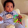 Charlene is registered to the contest to win money with this photo: baby, child, infant, onesie, toy, rattle, striped_clothing, sitting, indoor, couch, face, curly_hair, hand, seat, comfort, cute, expression, furniture, portrait, relaxing