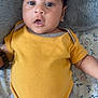 baby, infant, yellow_onesie, blanket, soft_texture, face, eyes, mouth, skin, arm, leg, lying_down, curious, indoors, floral_sheet, child, person, cute, expression, clothing