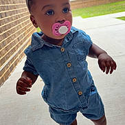 Kamorra is registered to the contest to win money with this photo: toddler, child, pacifier, denim, blue_outfit, sandals, headband, bow, outdoor, sidewalk, brick_wall, curious, standing, person, young_child, casual_clothing, daylight, portrait, footwear, concrete