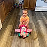 toddler, child, toy, ride_on_toy, minnie_mouse, pink, kitchen, flooring, wooden_floor, cabinet, stove, appliance, childrens_toy, indoor, person, clothing, short_sleeve_shirt, smile, play, curious