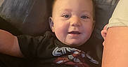 Skylar is registered to the contest to win money with this photo: baby, child, infant, drool, couch, sofa, black_shirt, graphic_tee, arm, skin, smile, happy, indoors, person, face, head, seated, relaxed, furniture, comfort