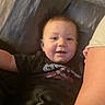 baby, child, infant, drool, couch, sofa, black_shirt, graphic_tee, arm, skin, smile, happy, indoors, person, face, head, seated, relaxed, furniture, comfort