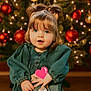 child, toddler, girl, christmas_tree, holiday, decorations, ornaments, lights, blue_eyes, pigtails, green_dress, indoor, smiling, festive, cute, holiday_season, portrait, floor, happy, celebration