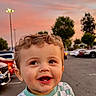 toddler, child, smiling, curly_hair, checkered_shirt, yin_yang, outdoor, parking_lot, cars, sunset, sky, trees, happy, person, cute, baby, expression, shopping_cart, evening, urban