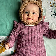 Emy a rejoint le concours — aidez-le/la à gagner de superbes lots ! baby, infant, child, face, hat, bear_ears, purple_clothing, striped_outfit, blanket, patterned_blanket, cute, lying_down, portrait, indoors, soft_texture, young_child, chubby_cheeks, smiling, cozy, warm_clothing