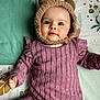 baby, infant, child, face, hat, bear_ears, purple_clothing, striped_outfit, blanket, patterned_blanket, cute, lying_down, portrait, indoors, soft_texture, young_child, chubby_cheeks, smiling, cozy, warm_clothing