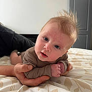 Yeva joined the competition — help win amazing prizes! baby, infant, hand, bed, bedspread, pattern, person, face, eyes, hair, skin, clothing, indoor, curious, lying_down, adult_hand, soft_light, closeup, portrait, expression