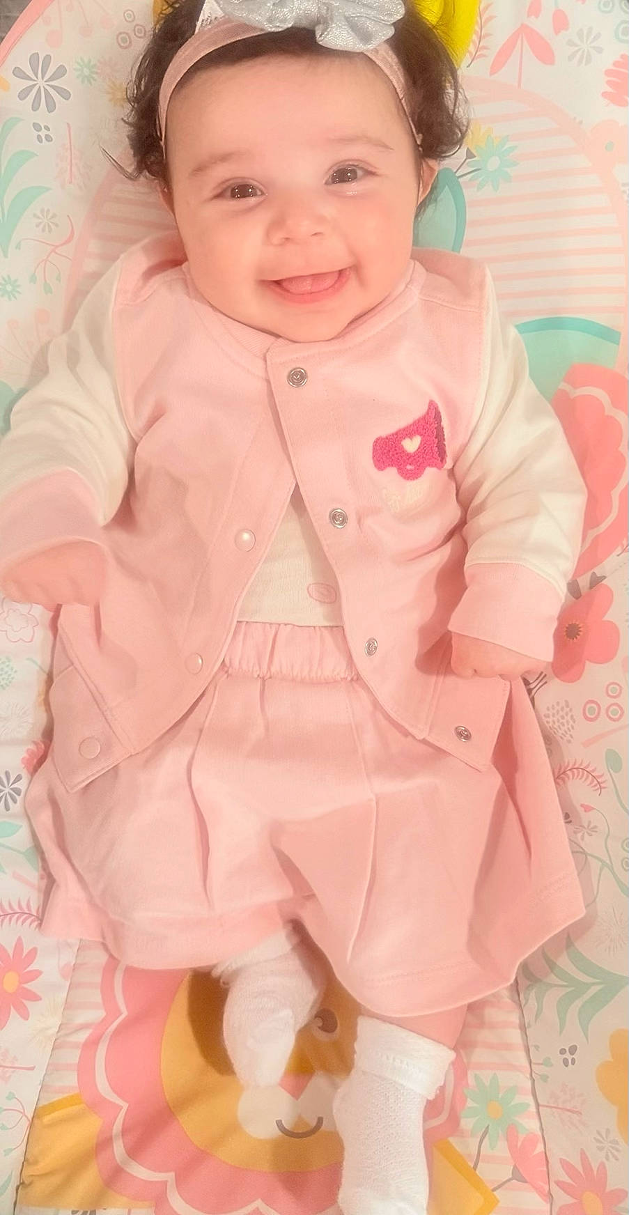 Marissa is registered to the contest to win money with this photo: baby, bow, child, clothing, colorful, cute, face, floral_mat, happy, headband, indoors, infant, lying_down, pants, photography, pink_outfit, play_mat, portrait, smiling, socks
