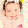 baby, child, infant, smiling, happy, portrait, face, headband, bow, pink_clothing, lying_down, blanket, patterned_background, indoor, close_up, dark_hair, brown_eyes, adorable, baby_photography, joy