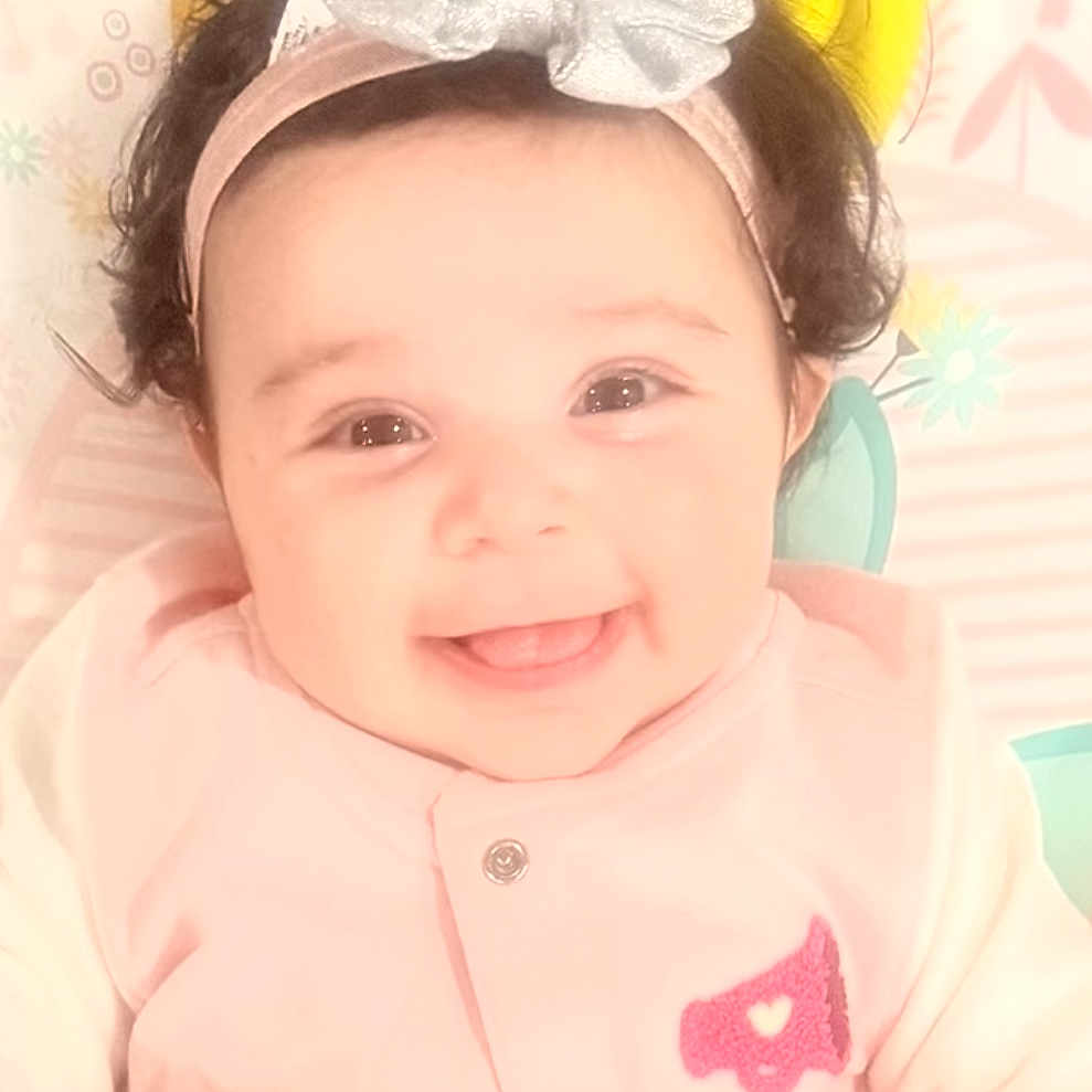 Marissa joined the competition — help win amazing prizes! baby, child, infant, smiling, happy, portrait, face, headband, bow, pink_clothing, lying_down, blanket, patterned_background, indoor, close_up, dark_hair, brown_eyes, adorable, baby_photography, joy