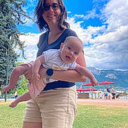 Anna participe au concours pour gagner de l'argent avec cette photo : woman, baby, child, outdoor, grass, sky, clouds, tree, glasses, shorts, tshirt, watch, red_umbrella, people, mountain, smile, happy, holding, tongue_out, park