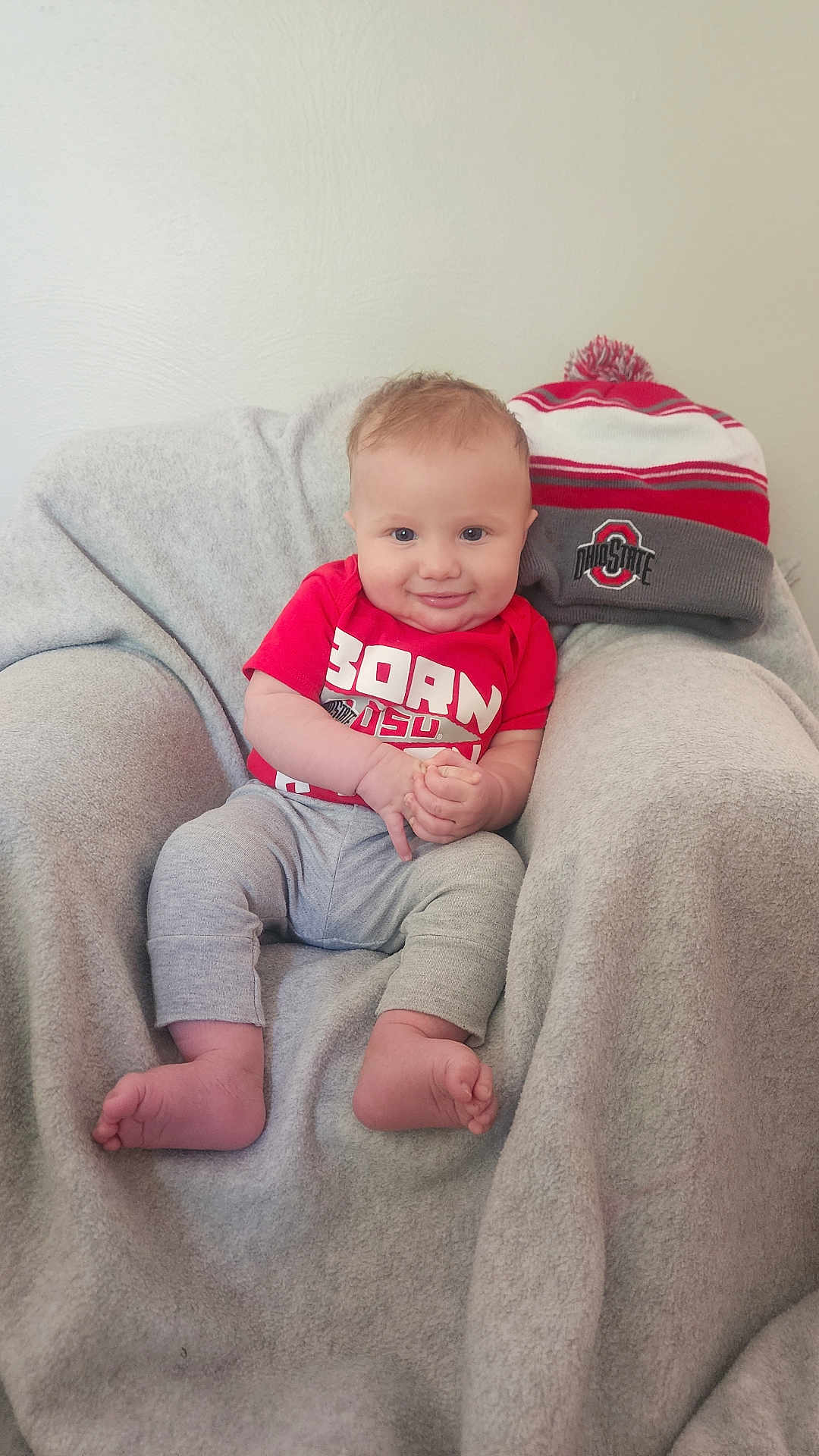 Austyn is registered to the contest to win money with this photo: baby, child, infant, smiling, red_shirt, grey_pants, beanie, hat, blanket, chair, indoors, cute, happy, portrait, sitting, feet, hands, face, cozy, soft