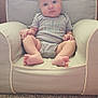armchair, baby, blue_eyes, carpet, child, chubby_cheeks, clothing, comfortable, cozy, cute, furniture, home, indoor, infant, onesie, person, portrait, sitting, soft_lighting, wood_paneling