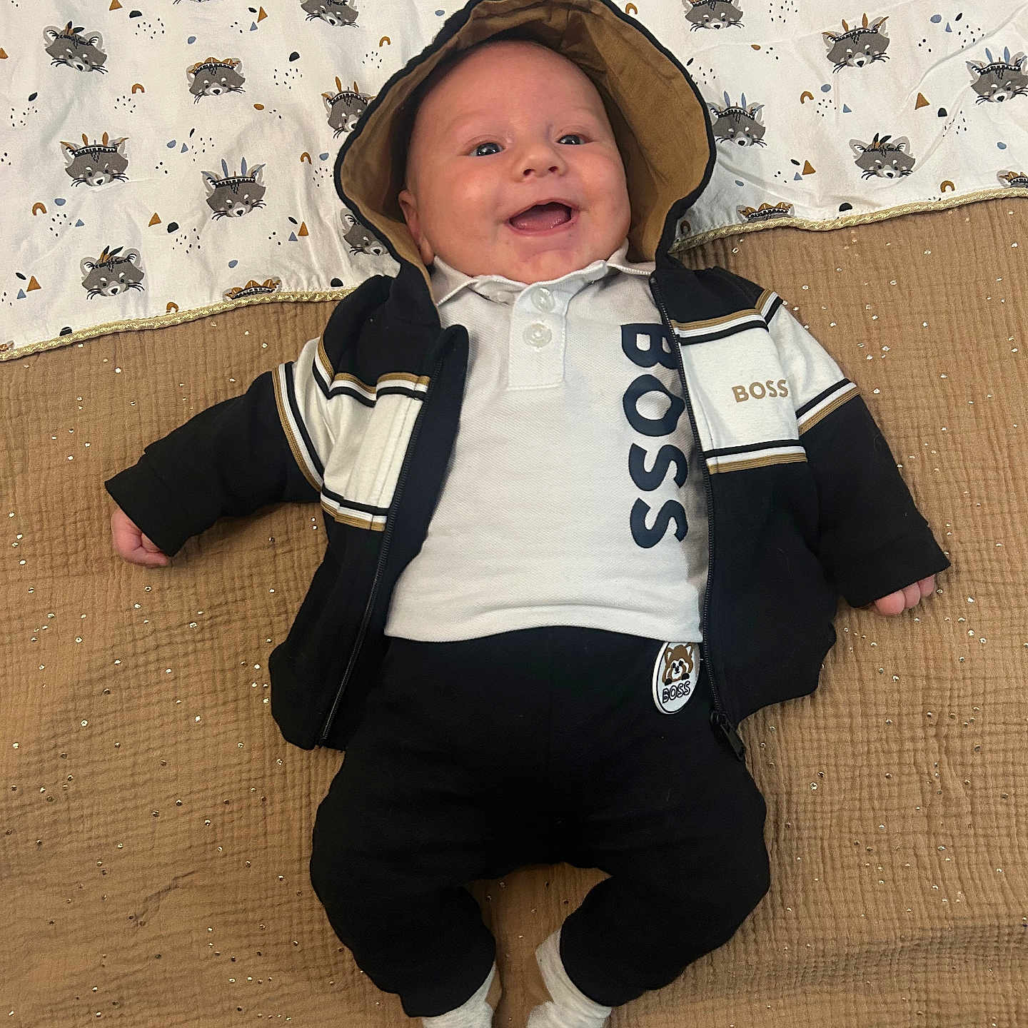 Rafaël participe au concours pour gagner de l'argent avec cette photo : baby, blanket, casual, child, clothing, comfortable, cute, cute_outfit, happy, hoodie, indoors, infant, jacket, lying_down, pattern, person, portrait, raccoon, smiling, socks