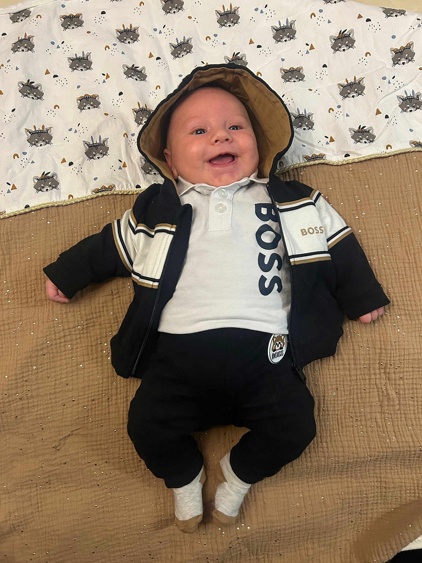 Rafaël participe au concours pour gagner de l'argent avec cette photo : baby, child, smiling, hoodie, jacket, blanket, pattern, raccoon, clothing, socks, cute, happy, infant, person, lying_down, casual, portrait, indoors, comfortable, cute_outfit