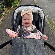 Miley is registered to the contest to win money with this photo: baby, baby_girl, blanket, child, clothing, cute, daytime, happy, headband, infant, outdoor, person, pink_bow, sidewalk, smile, street, stroller, toy, unicorn, urban