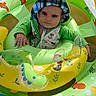 baby, child, child_in_float, colorful, cute, dinosaur_print, floating, green_clothing, hat, infant, inflatable_float, outdoor, playtime, pool, smiling, summer, sun_hat, sunny_day, water, yellow_canopy