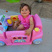 Nayeli is registered to the contest to win money with this photo: toddler, child, toy_car, pink, outdoor, smiling, happy, plastic_toy, playground, concrete, brick_wall, spring_rider, dog_toy, casual_clothing, short_sleeves, sunlight, fun, playtime, young_child, portrait