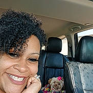Cookie joined the competition — help win amazing prizes! car_interior, car_seat, casual, colorful_clothing, curly_hair, dog, flower_accessory, hand, happy, jewelry, leather_seat, nose_ring, passenger, pet, portrait, relaxed, small_dog, smile, vehicle, woman
