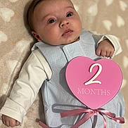 Maybel a rejoint le concours — aidez-le/la à gagner de superbes lots ! baby, infant, face, eyes_open, chubby_cheeks, blanket, heart_shape, milestone_sign, pink, blue, ribbon, sleep_sack, onesie, lying_down, portrait, close_up, hand, cute, soft_texture, indoor