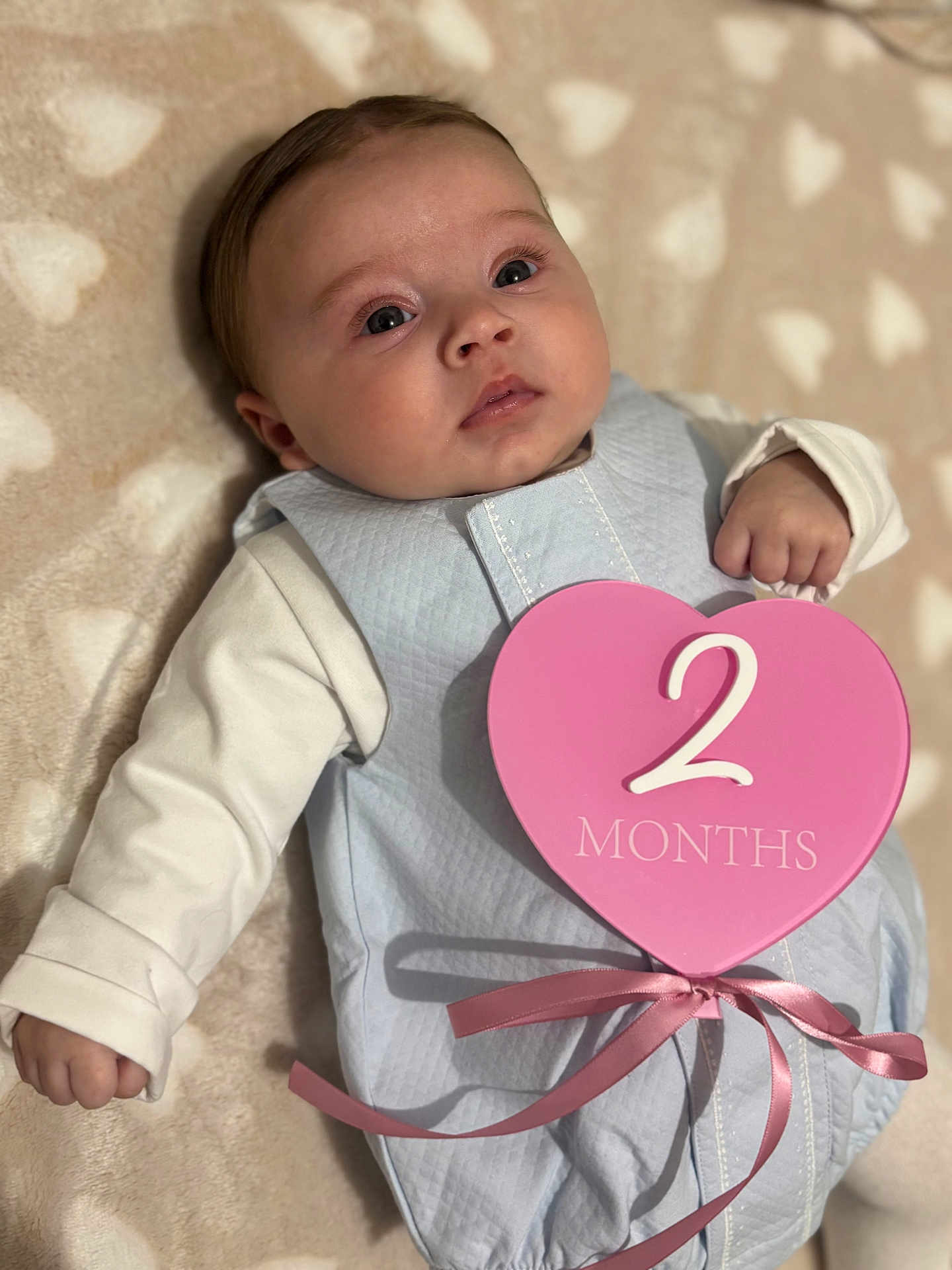 Maybel a rejoint le concours — aidez-le/la à gagner de superbes lots ! baby, infant, face, eyes_open, chubby_cheeks, blanket, heart_shape, milestone_sign, pink, blue, ribbon, sleep_sack, onesie, lying_down, portrait, close_up, hand, cute, soft_texture, indoor