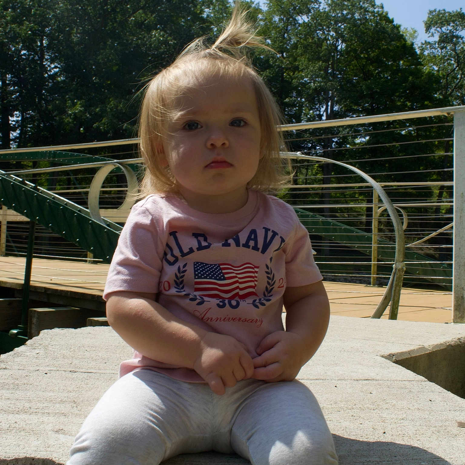 Paisley is registered to the contest to win money with this photo: baby, clothing, face, grass, handrail, head, jeans, nature, outdoors, pants, park, person, photography, plant, playarea, portrait, railing, sitting, t_shirt, wood