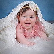 Skye joined the competition — help win amazing prizes! baby, child, smiling, pink_dress, headband, flower, blanket, white, fluffy, soft_texture, blue_background, happy, cute, portrait, infant, lying_down, close_up, face, skin, innocence