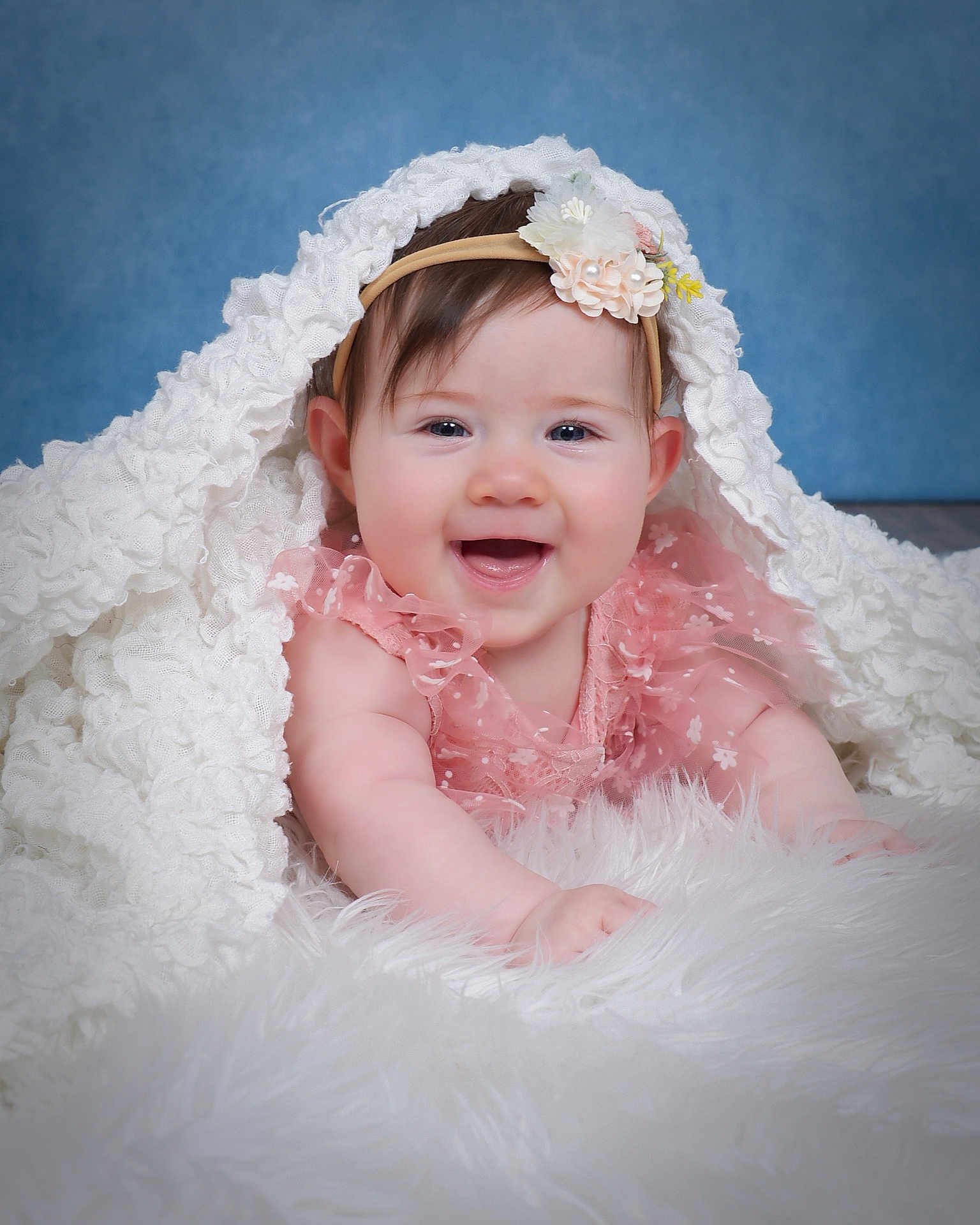 Skye joined the competition — help win amazing prizes! baby, child, smiling, pink_dress, headband, flower, blanket, white, fluffy, soft_texture, blue_background, happy, cute, portrait, infant, lying_down, close_up, face, skin, innocence