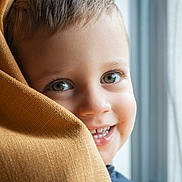 Elio participe au concours pour gagner de l'argent avec cette photo : toddler, child, smile, face, eyes, blanket, window, curtain, happy, close_up, portrait, indoors, cozy, soft_light, fabric, skin, cute, baby, person, young