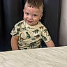 toddler, child, smiling, dinosaur_shirt, marble_table, black_cushion, short_hair, indoors, cute, portrait, sitting, happy, playful, young_child, person, casual_clothing, background, head, face, eyes