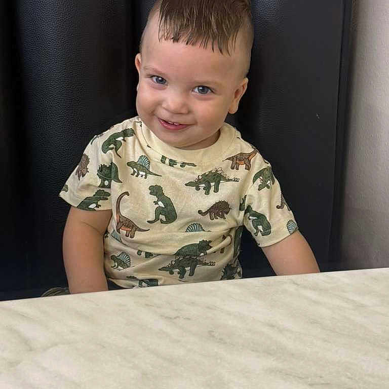 Riann is registered to the contest to win money with this photo: toddler, child, smiling, dinosaur_shirt, marble_table, black_cushion, short_hair, indoors, cute, portrait, sitting, happy, playful, young_child, person, casual_clothing, background, head, face, eyes
