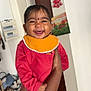 baby, child, smiling, indoor, person, arm, clothing, red_outfit, orange_bib, face, happy, holding, painting, wall, door, earrings, home, wood_floor, furniture, socks