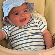 Jonas a rejoint le concours — aidez-le/la à gagner de superbes lots ! baby, child, smiling, hat, striped_shirt, high_chair, indoor, cute, tongue_out, happy, portrait, infant, clothing, face, person, seat, seat_cushion, skin, headwear, baby_furniture