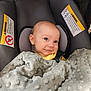 baby, car_seat, blanket, smile, infant, child, face, head, yellow_clothing, gray_blanket, warning_label, seat_belt, indoor, cute, portrait, person, cozy, young_child, happy, seated