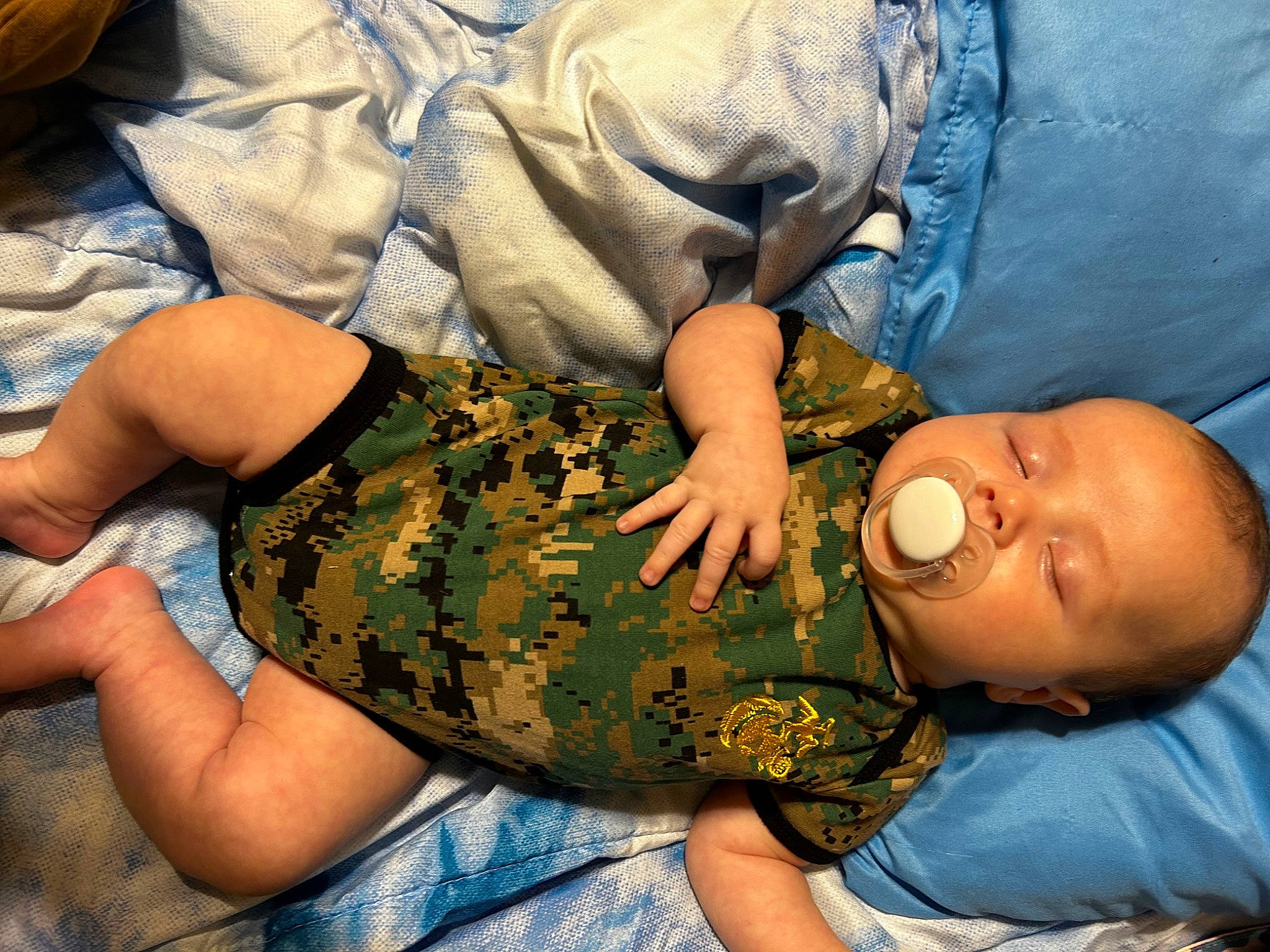 Kooper is registered to the contest to win money with this photo: baby, camouflage, child, comfort, elbow, finger, gesture, grass, human_leg, joint, knee, military_camouflage, nail, pattern, person, sitting, t_shirt, thigh, thumb, toddler