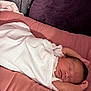 newborn, baby, sleeping, blanket, white_clothing, pink_cushion, soft_texture, infant, peaceful, resting, cozy, portrait, indoor, child, cute, wrapped, relaxed, small_hands, face, head