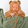Hamza is registered to the contest to win money with this photo: newborn, baby, sleeping, knitted_clothing, bear_ears, hoodie, blanket, bed, cozy, cute, infant, soft_texture, hand, face, peaceful, portrait, child, warm, resting, indoors