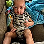 baby, infant, child, camo_onesie, couch, blanket, blue_blanket, brown_couch, indoors, person, cute, face, legs, hands, relaxed, seated, soft_light, home, comfort, curious