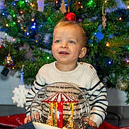 Mylo a rejoint le concours — aidez-le/la à gagner de superbes lots ! child, toddler, christmas_tree, holiday, snow_globe, decorations, lights, festive, smile, sweater, striped_clothing, indoors, toy, happy, seasonal, celebration, face, person, joy, winter