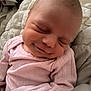 baby, infant, newborn, sleeping, smiling, close_up, pink_clothing, onesie, blanket, bedding, soft_texture, bald_head, face, cheek, tiny_mouth, peaceful, portrait, cute, arm, cozy