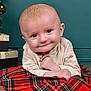 baby, infant, smile, face, plaid_blanket, beige_shirt, blue_eyes, gift_boxes, christmas_ornaments, wooden_floor, green_wall, portrait, cute, child, holiday, indoor, closeup, happy, crawling, young_child