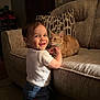 toddler, child, cat, couch, indoor, smile, pet, furniture, home, window, curtain, pillow, clothing, person, animal, happy, light, face, standing, collar
