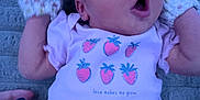 Fiona is registered to the contest to win money with this photo: apparel, baby, blanket, child, cute, expression, face, hand, infant, lying_down, mittens, mouth_open, newborn, onesie, person, pink_clothing, skin, soft_texture, strawberry, young