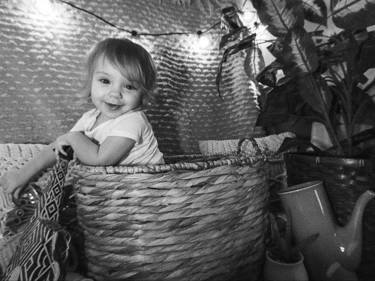 Evie is registered to the contest to win money with this photo: basket, black, black_and_white, child, comfort, flash_photography, flowerpot, happy, houseplant, joy, monochrome, monochrome_photography, person, plant, room, sitting, smile, still_life_photography, storage_basket, style