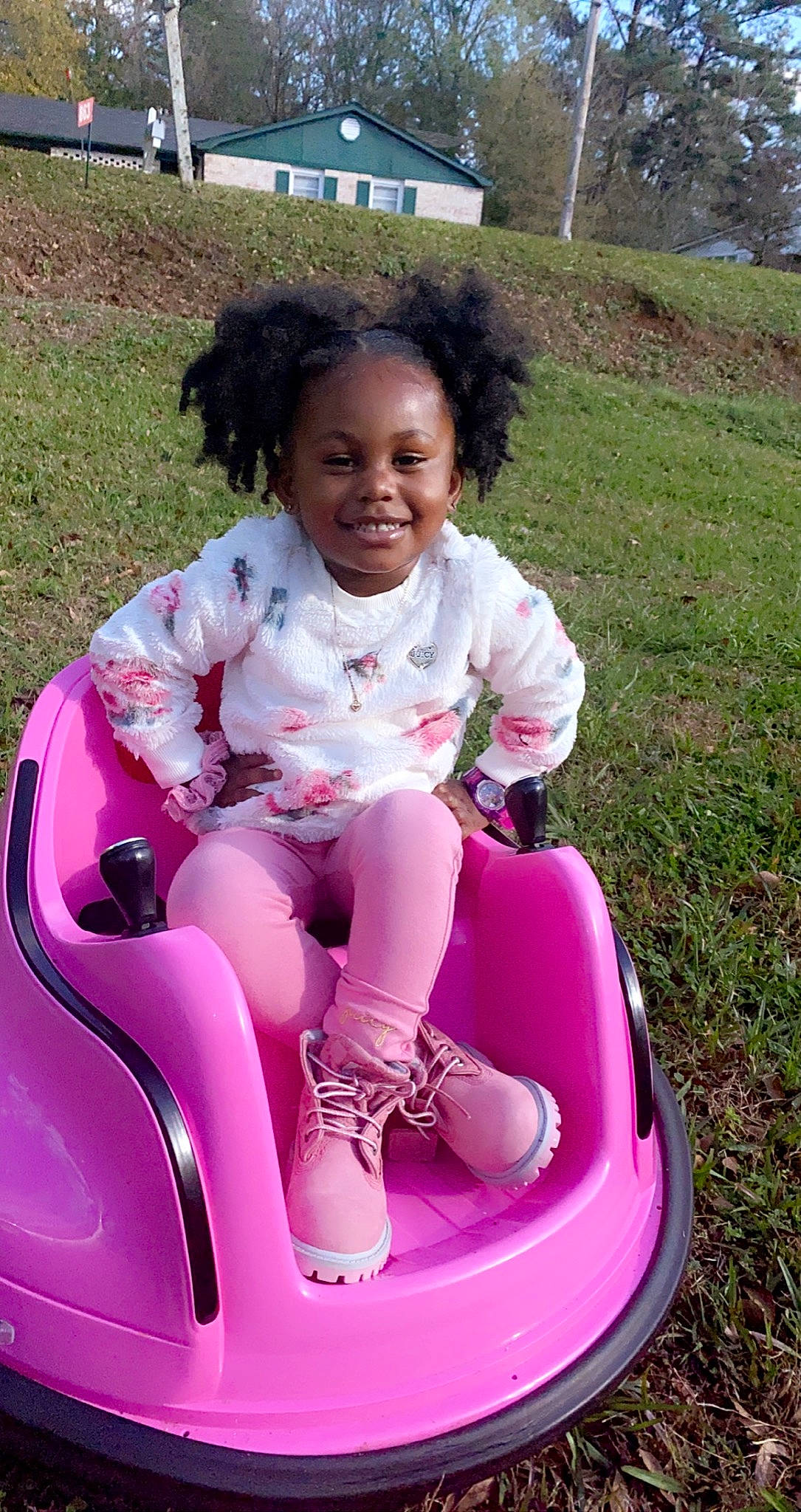 Cori is registered to the contest to win money with this photo: baby_toddler_clothing, child, face, facial_expression, fun, grass, hair, happy, head, joy, lap, leisure, magenta, person, pink, plant, recreation, riding_toy, shorts, sitting