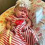 baby, sleeping, dress, flower_headband, striped_clothing, infant, child, cushion, floral_pattern, peaceful, napping, indoor, cute, small_hands, small_feet, headwear, soft_lighting, portrait, resting, adorable