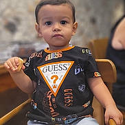 Isaac a rejoint le concours — aidez-le/la à gagner de superbes lots ! black_tshirt, boy, bread, casual_clothing, child, expressionless, face, food, furniture, guess_logo, holding, indoor, person, portrait, shorts, sitting, table, toddler, wooden_chair, young_child