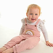 Myla joined the competition — help win amazing prizes! barefoot, blonde_hair, blue_eyes, bright_background, child, curly_hair, cute, fashion, happy, indoors, long_sleeve, pink_overalls, playful, portrait, rainbow_patch, sitting, smiling, studio, toddler, white_shirt