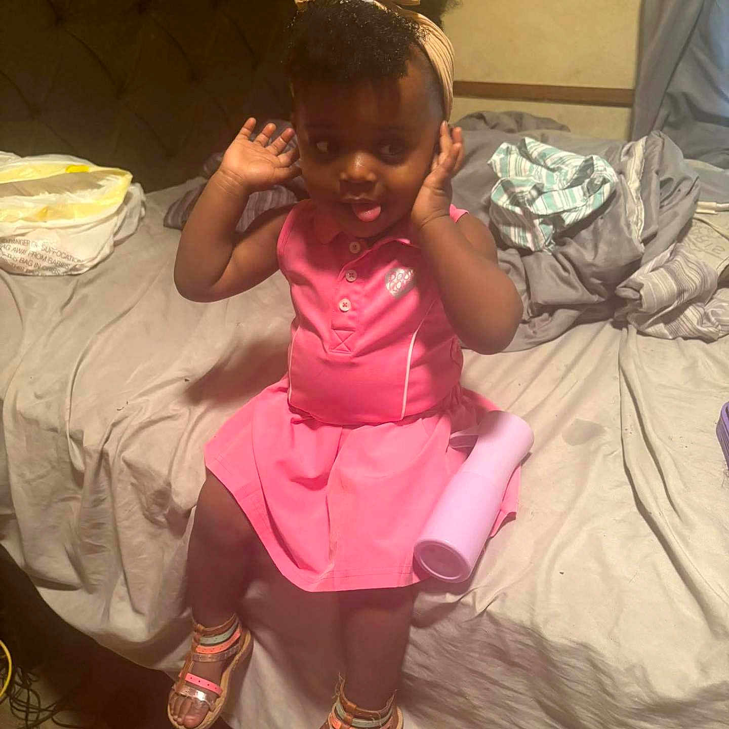 Riiver is registered to the contest to win money with this photo: toddler, child, pink_dress, sandals, bed, bottle, headband, hands, tongue_out, indoors, messy_bed, blanket, curtain, floor, furniture, person, cute, playful, hair, skin