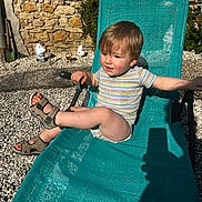 Gabin participe au concours pour gagner de l'argent avec cette photo : toddler, child, outdoor, sunlight, chair, sandals, stone_wall, garden_gnomes, playful, smiling, summer, relaxing, striped_shirt, legs, hand, shadow, gravel, green_chair, portrait, daytime